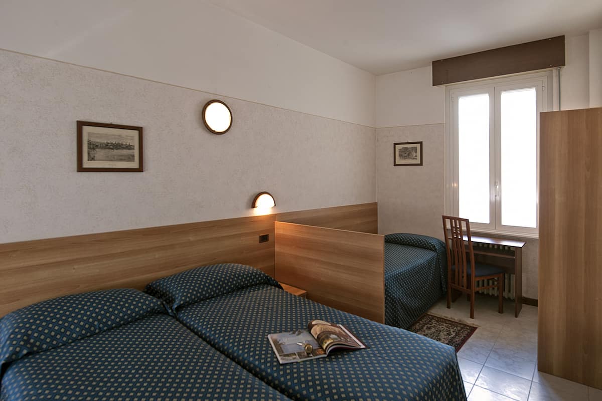 Habitación de hotel con cama, escritorio y silla. Dos cuadros decoran la pared.