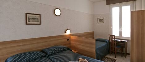 Habitación de hotel con cama, escritorio y silla. Dos cuadros decoran la pared.