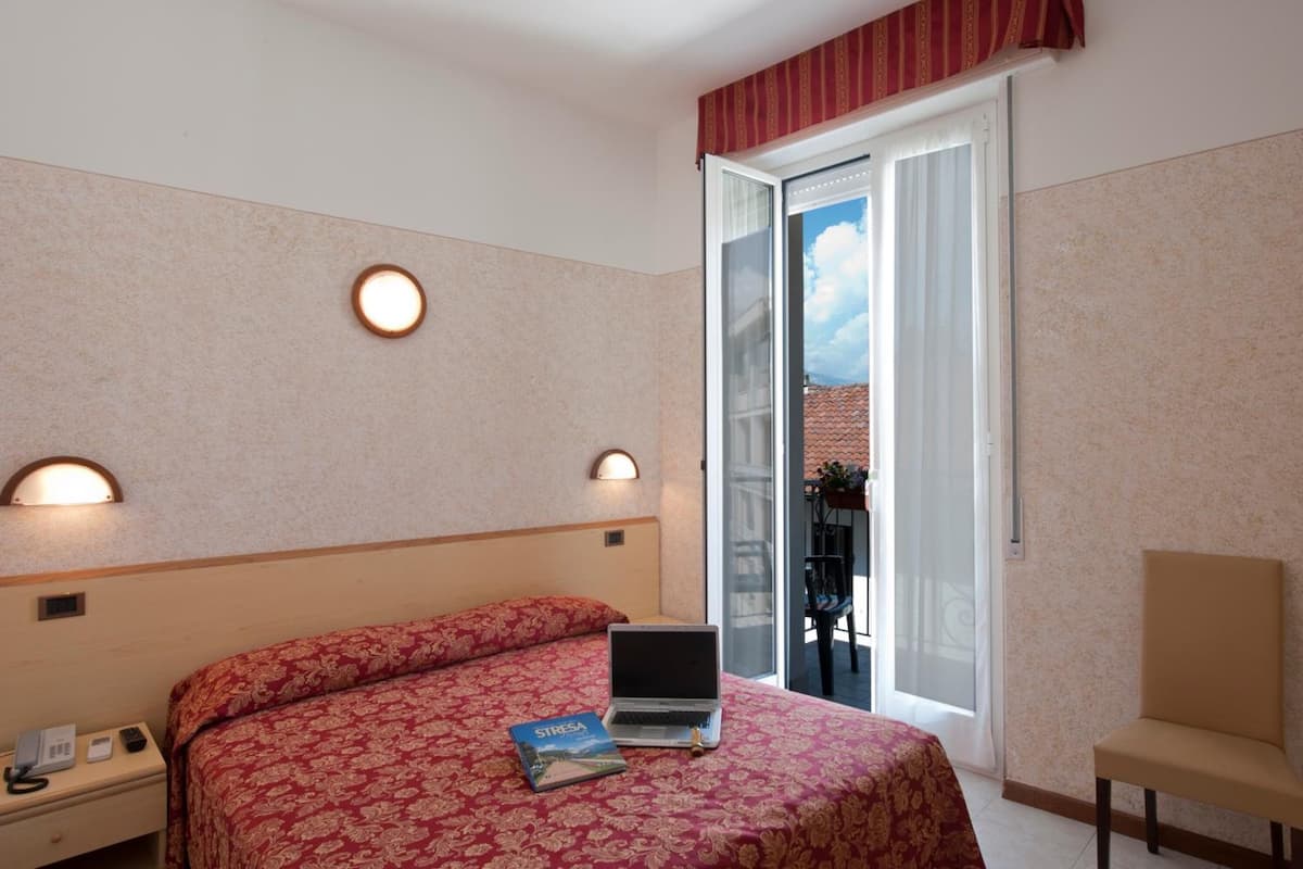 Una habitación de hotel con cama, laptop, mesita de noche con teléfono y una silla.