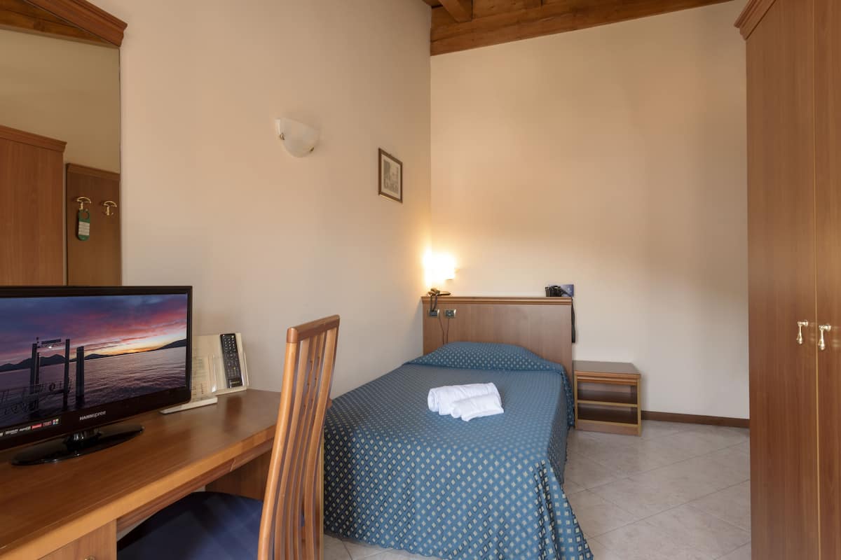 Una habitación de hotel con cama, escritorio con televisor, mesita de noche y armario de madera.