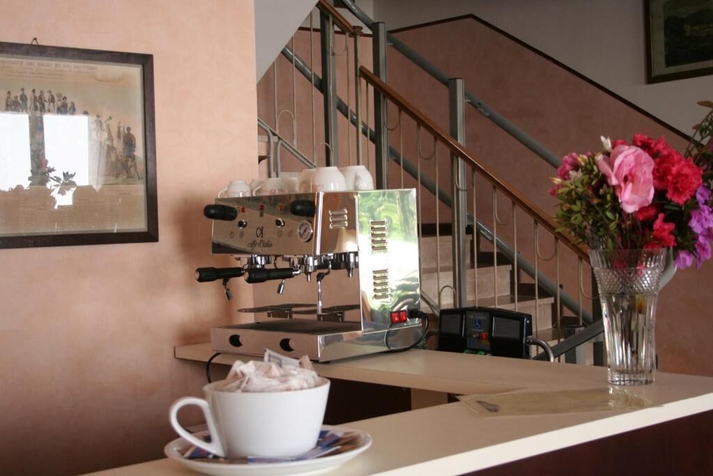 A coffee machine, a cup of coffee, and a vase of flowers on a counter.