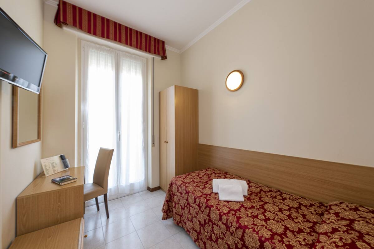 Una habitación de hotel con cama, escritorio, silla, televisión y armario.