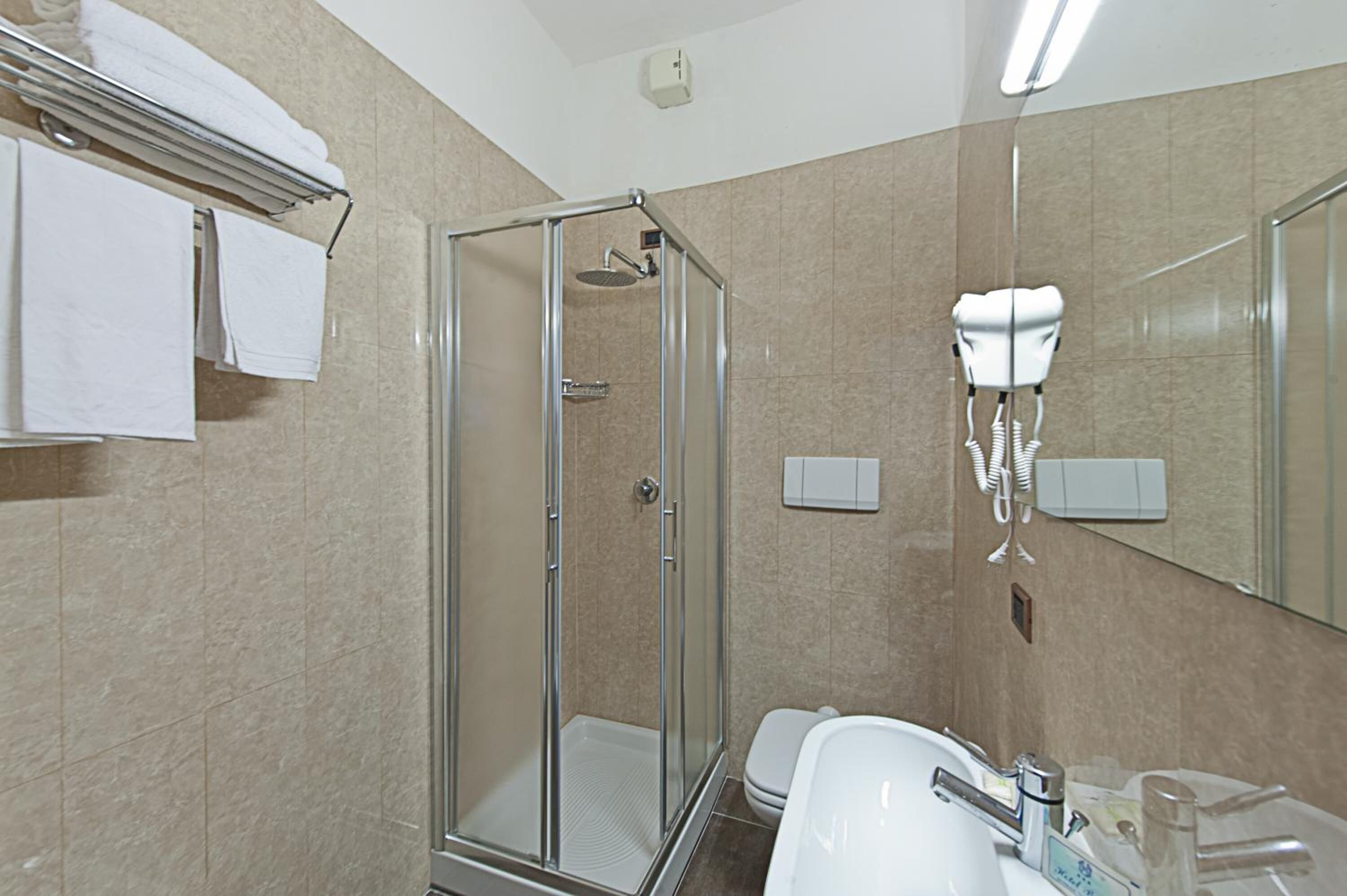 A bathroom with a glass-enclosed shower, a sink with a mirror, and a hairdryer mounted on the wall.