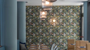 A restaurant with a long dining table, blue upholstered seating, and a floral wallpaper.