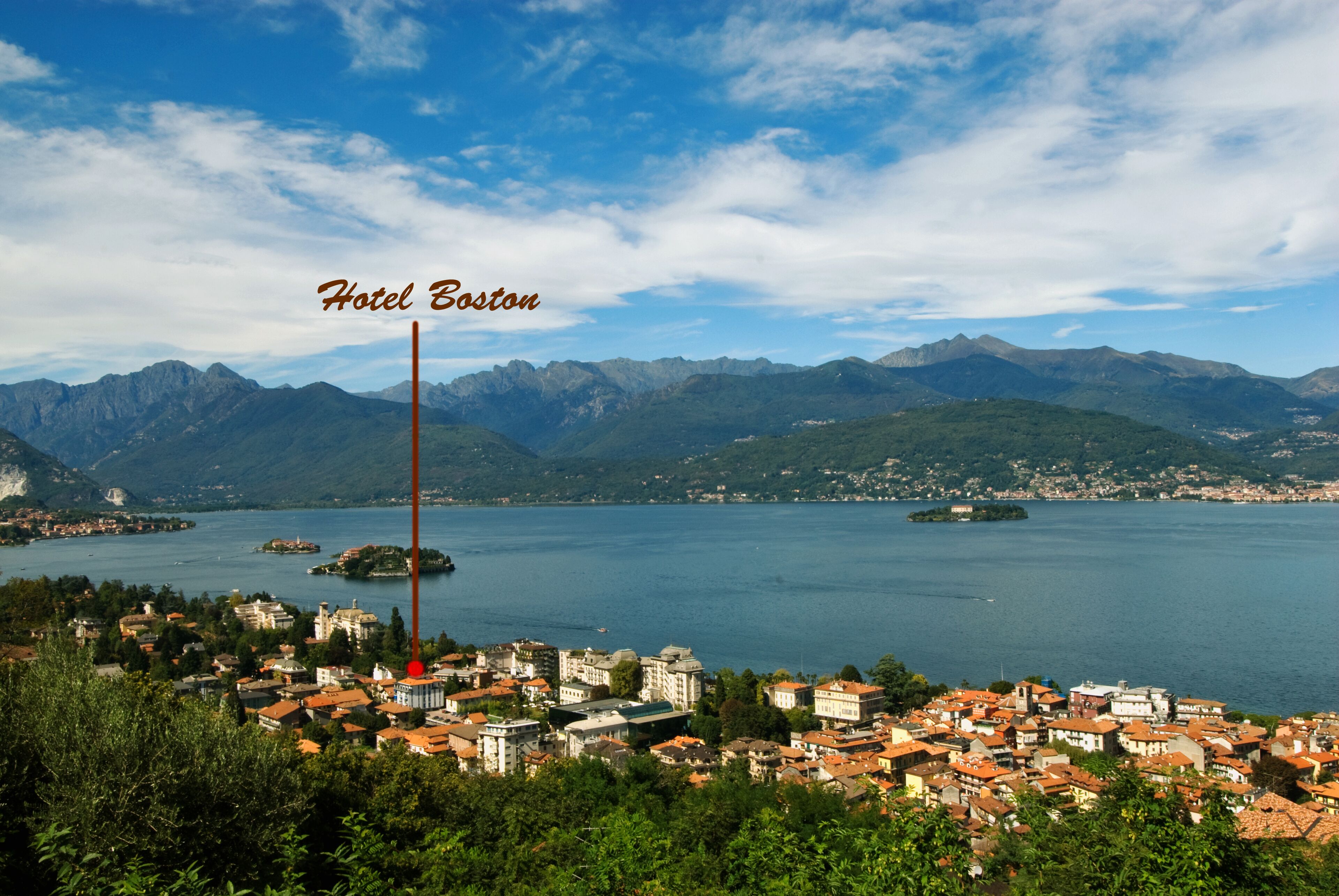 Una località costiera con un cartello ben visibile dell'Hotel Boston, circondata da montagne e un lago.