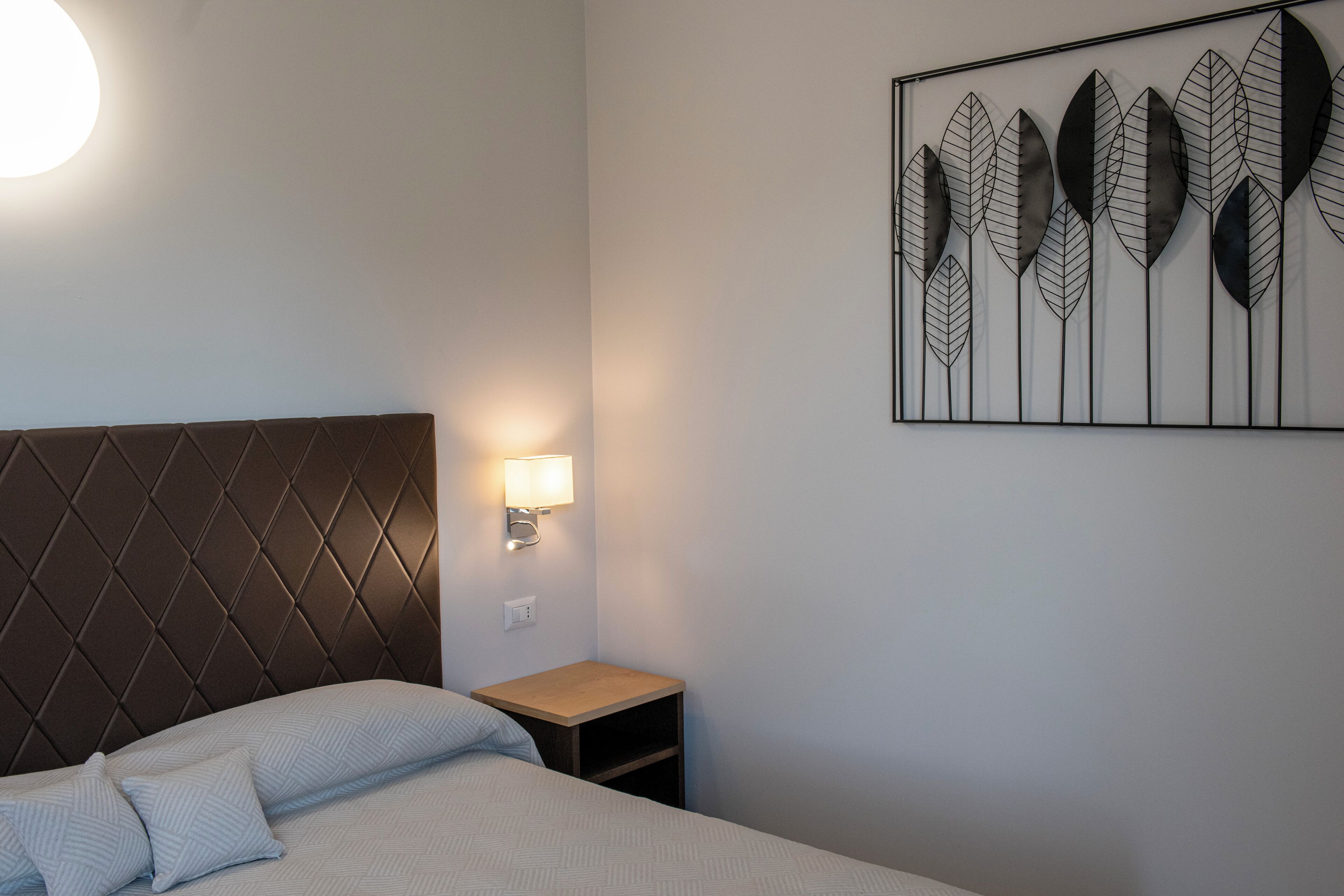 A neatly made bed with a headboard, a bedside table with a lamp, and a wall art piece.