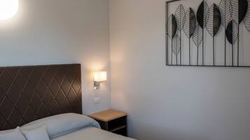 Un lit bien fait, avec une tête de lit, une table de chevet avec une lampe et une œuvre d’art accrochée au mur.