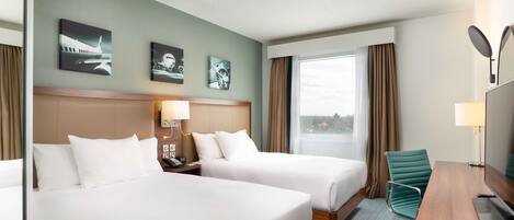Ein Hotelzimmer mit zwei Betten, einem Schreibtisch, einem Stuhl und einem großen Fenster.