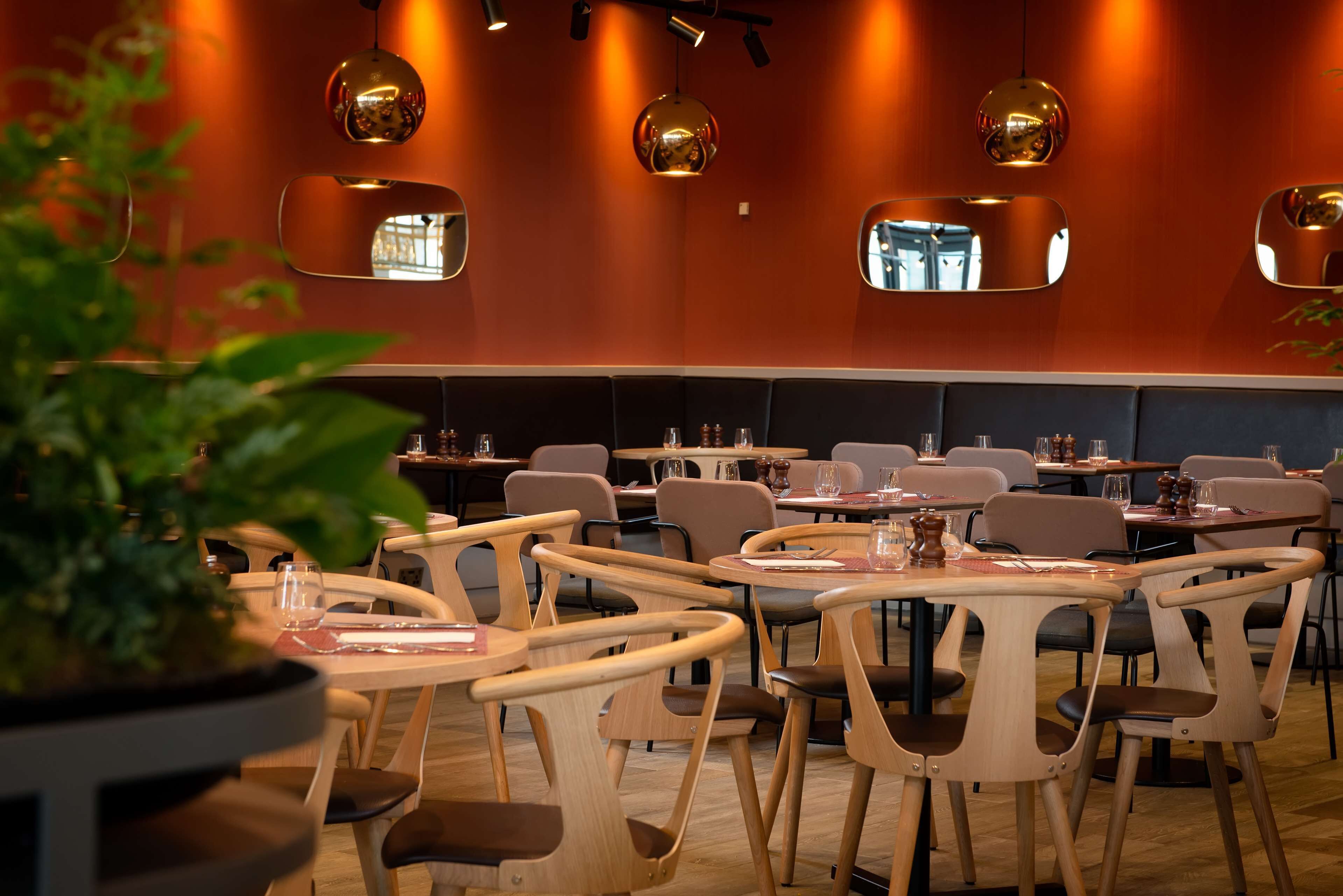 Um restaurante com mesas e cadeiras redondas, um vaso de planta e luminárias pendentes.