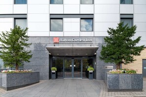 The entrance of a Hilton Garden Inn with a modern facade, large glass doors, and potted plants on either side. - Hilton Garden Inn London Heathrow Airport (Hounslow)