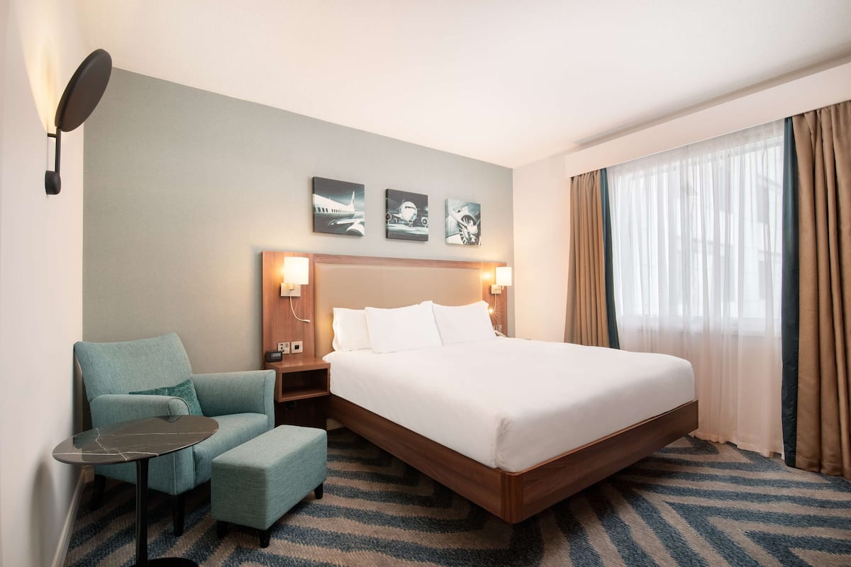 Una camera d'albergo con un letto grande, una sedia, un tavolino e un comodino. Sopra il letto si trovano tre quadri appesi al muro.