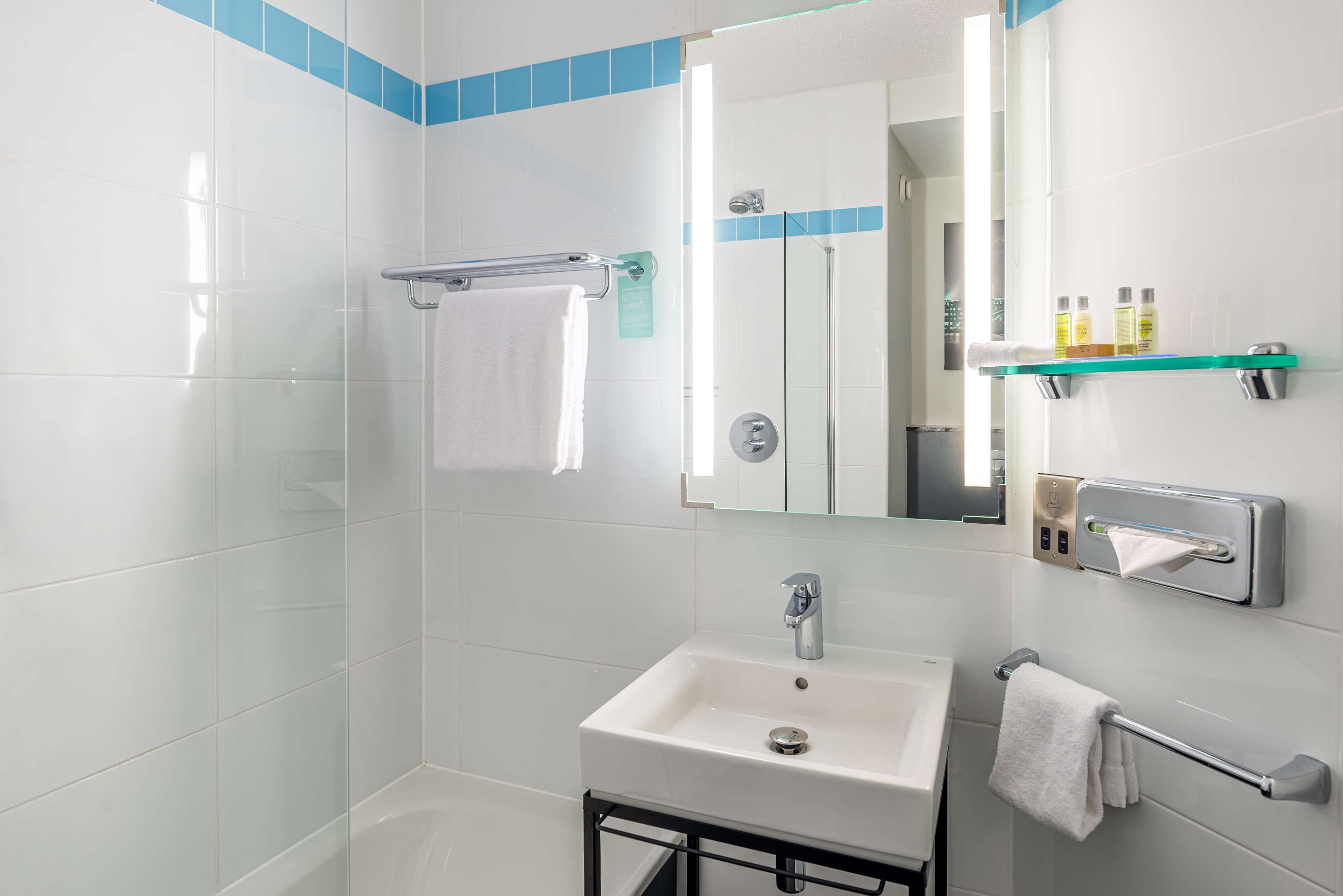 A modern bathroom with a white sink, a glass shower enclosure, and a mirror with a towel rack.