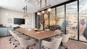 A conference room with a long table, chairs, a television, and a large window with a map and writings.