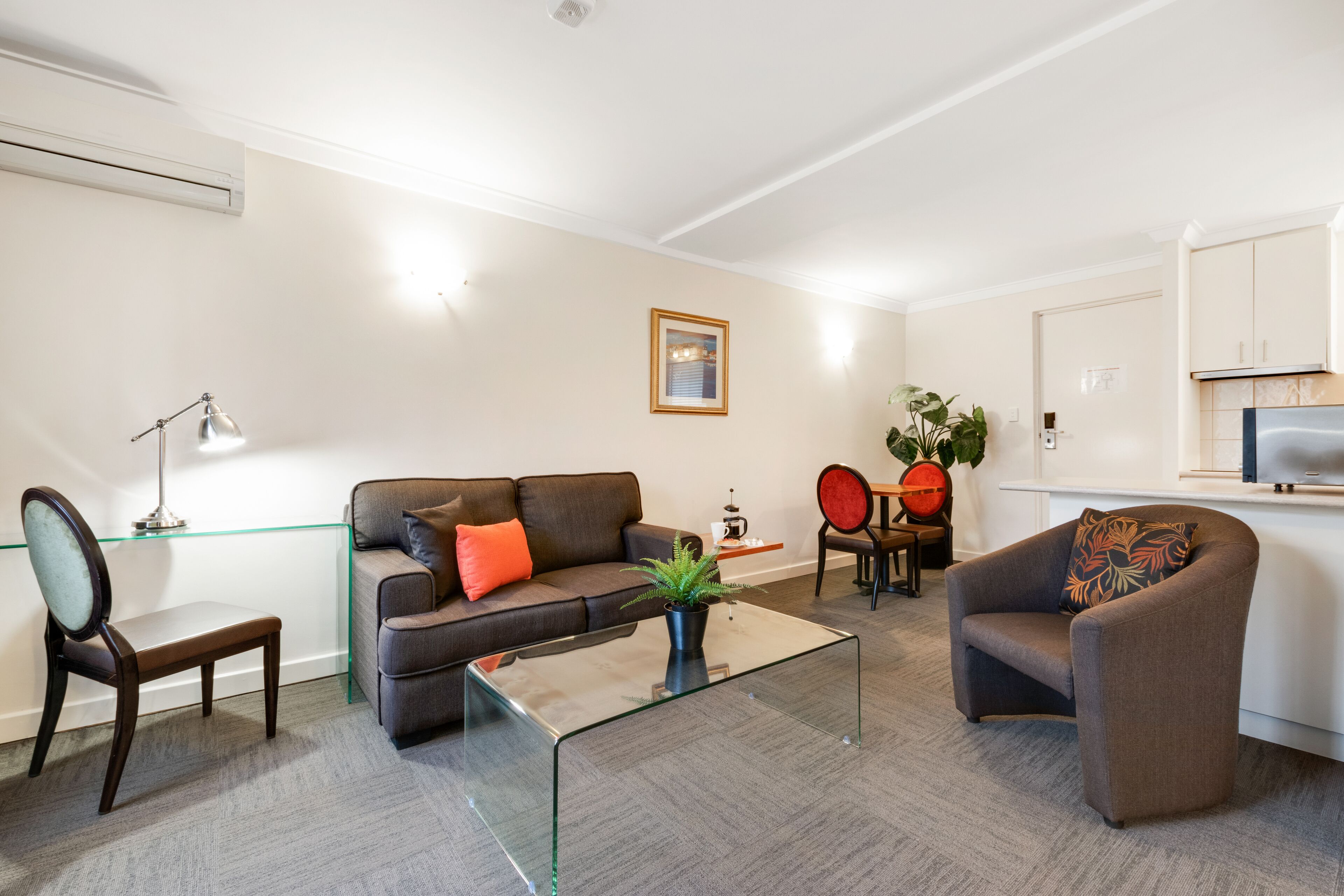 Un salon moderne avec une table basse en verre, un canapé, un fauteuil et un petit coin repas.