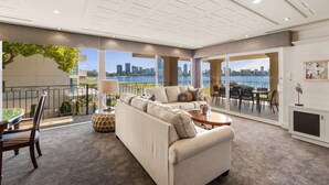 A spacious living area with a large sofa, a coffee table, and a view of the city skyline through large windows. - The Peninsula Riverside Serviced Apartments (South Perth)