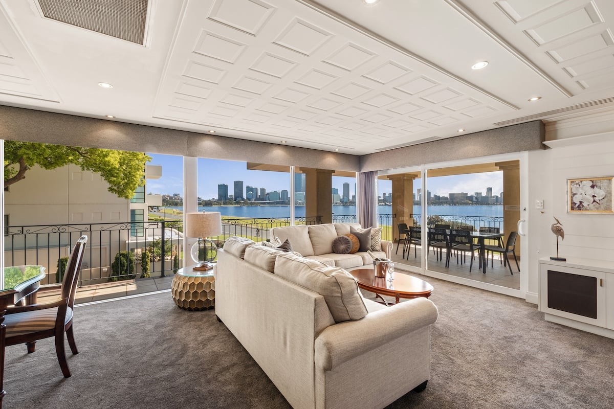 A spacious living area with a large sofa, a coffee table, and a view of the city skyline through large windows.
