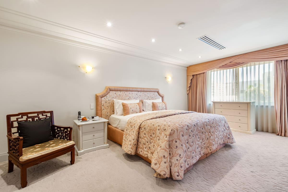 A bedroom with a large bed, a nightstand, a wooden bench, and a dresser.