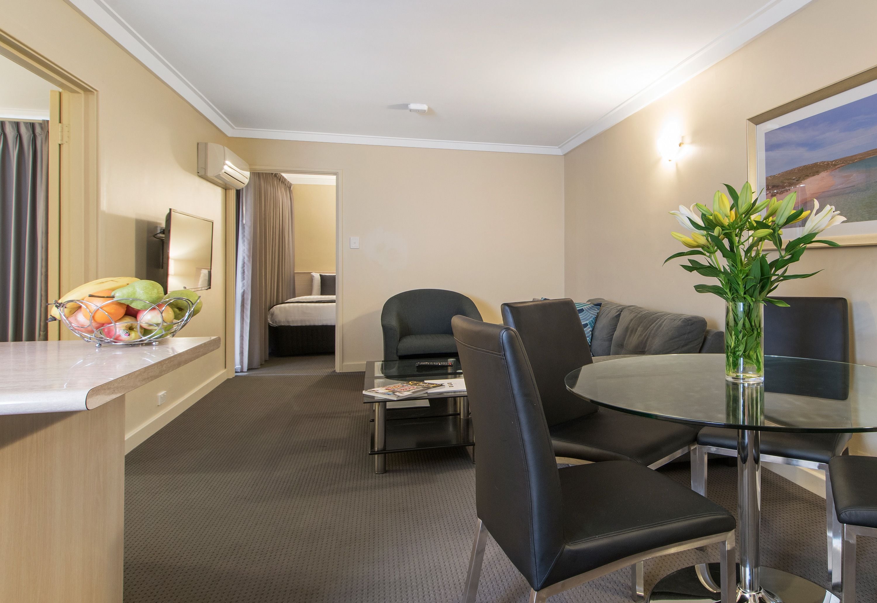 A hotel room with a dining area, a glass table, and a fruit bowl.
