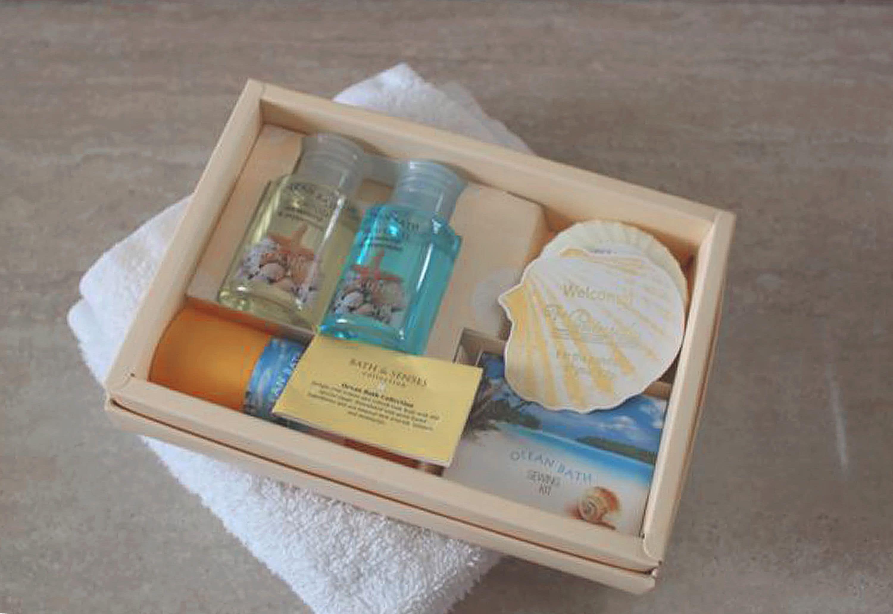 Una caja de madera con productos de baño y cuidado corporal, como una botella de loción, un recipiente con jabón y una concha decorativa.