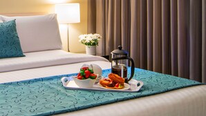 A neatly made bed with a tray of breakfast items, including pastries and a bowl of fruit. - The Peninsula Riverside Serviced Apartments (South Perth)