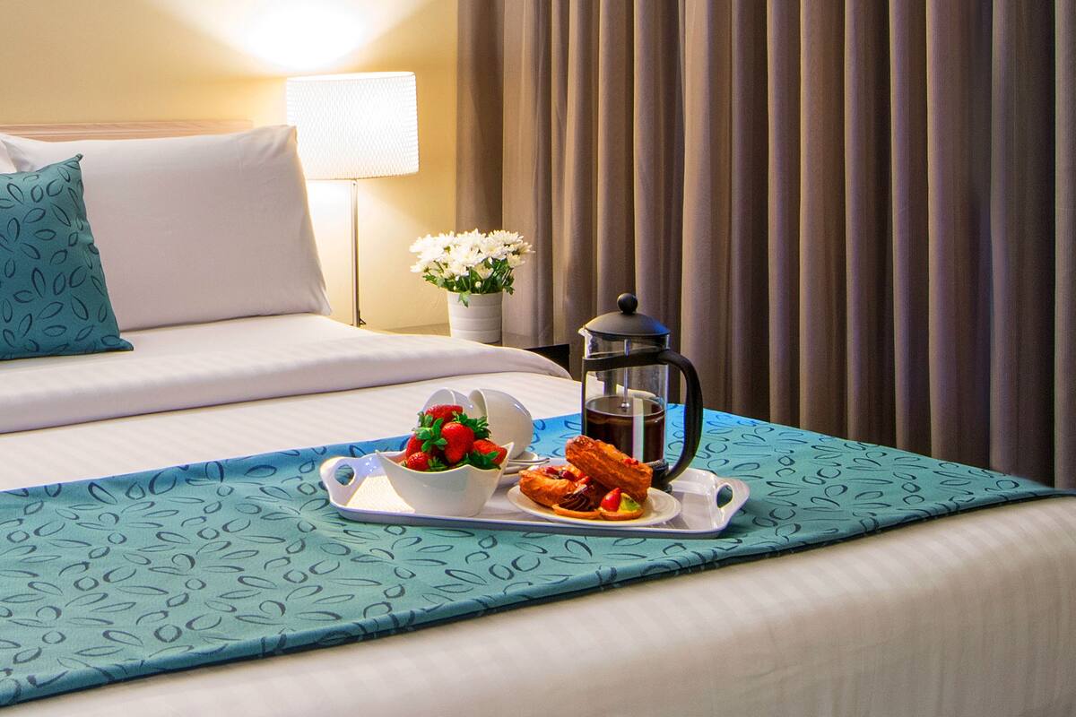 A neatly made bed with a tray of breakfast items, including pastries and a bowl of fruit.