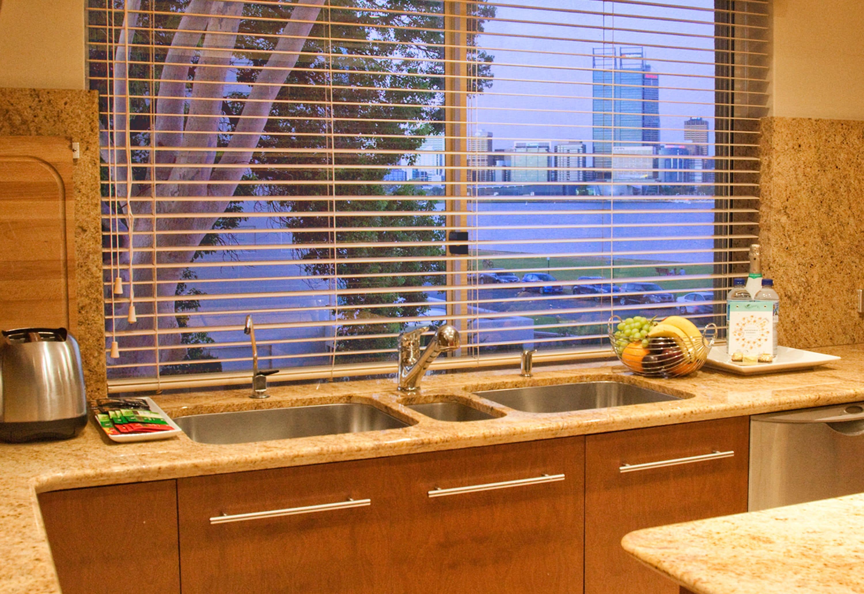 A kitchen with two sinks, wooden cabinets, a coffee maker, and a window with blinds.
