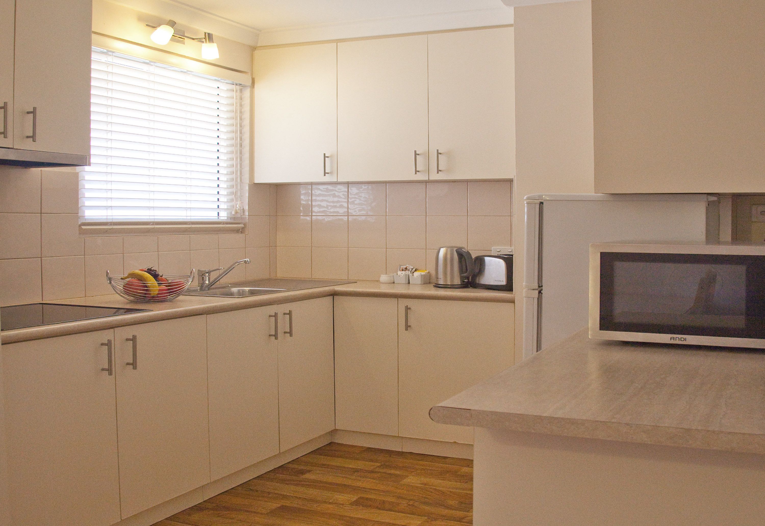 A kitchen with white cabinets, a stainless steel sink, a microwave, and a fruit bowl on the counter.
