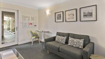 A modern living room with a grey sofa, patterned cushions, a small table, and framed pictures on the wall.