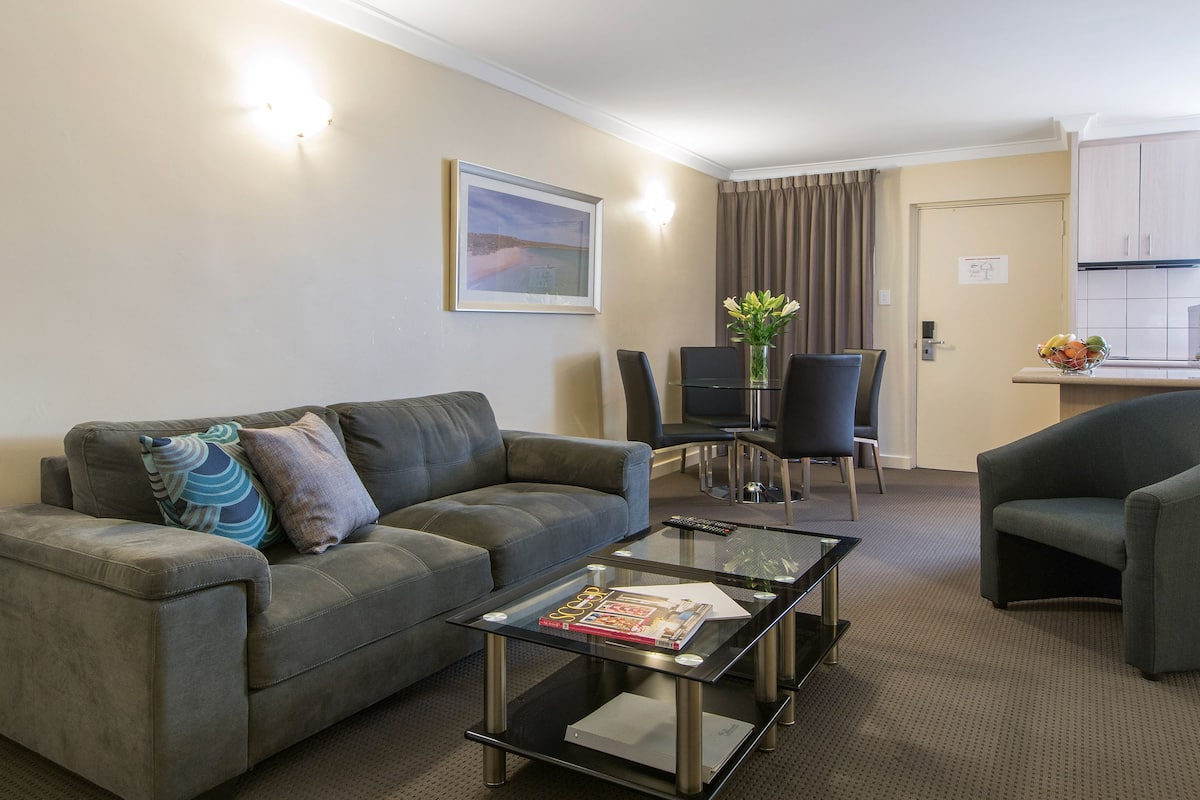 A modern living room with a sofa, a glass coffee table, and a dining area with a table and chairs.