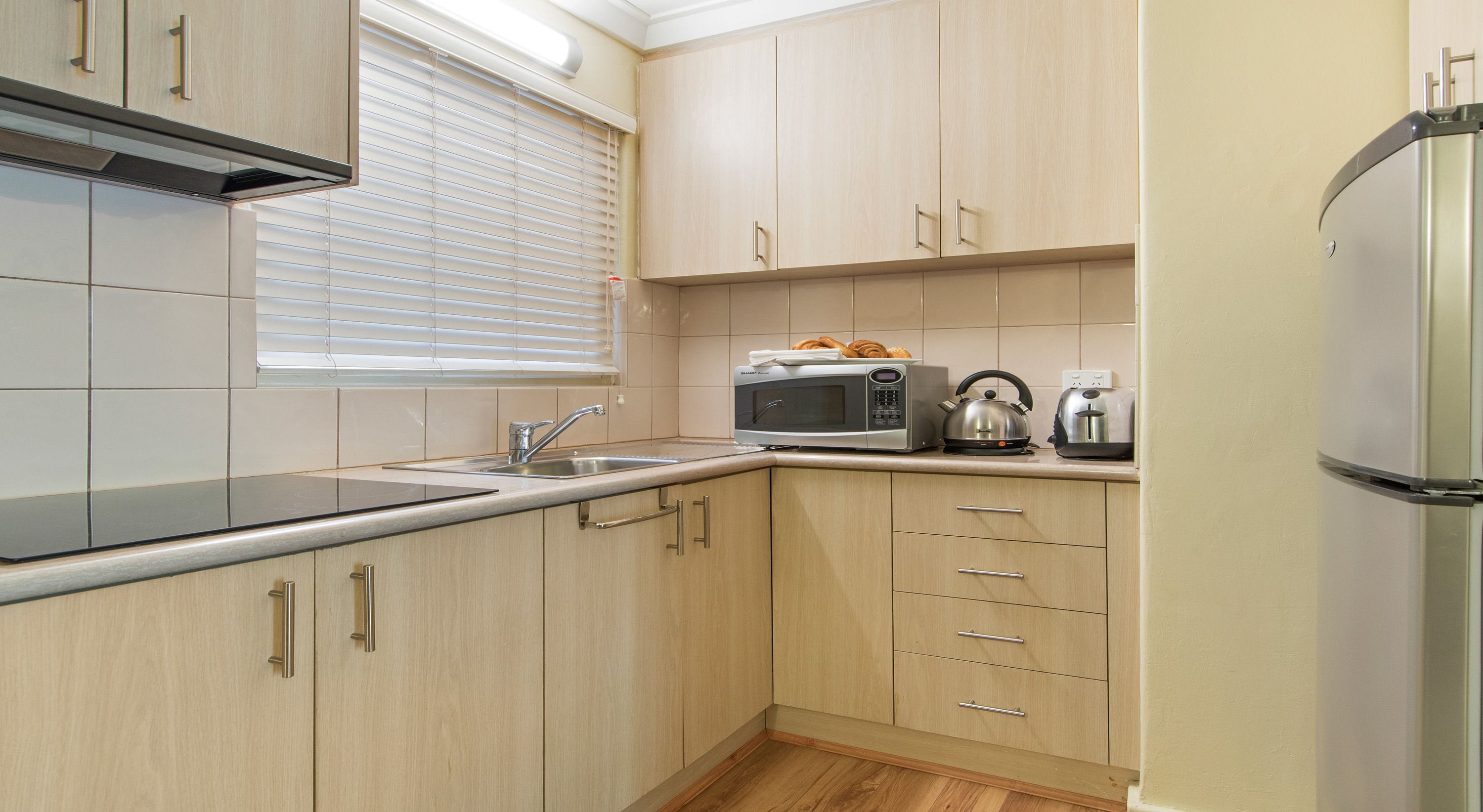 Una cocina moderna con armarios de madera clara, un lavamanos de acero inoxidable, microondas, hervidor y tostadora.