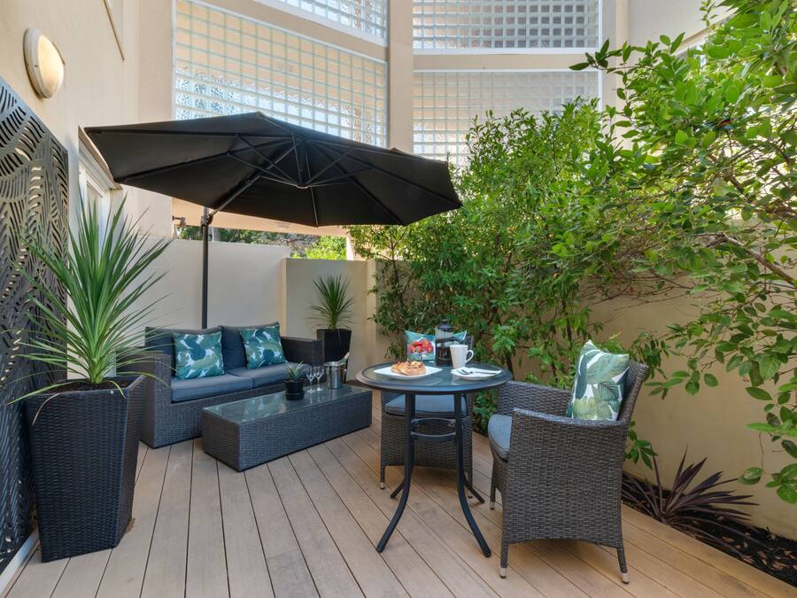 Un patio al aire libre con un sofá, sillas, una mesa y una sombrilla.