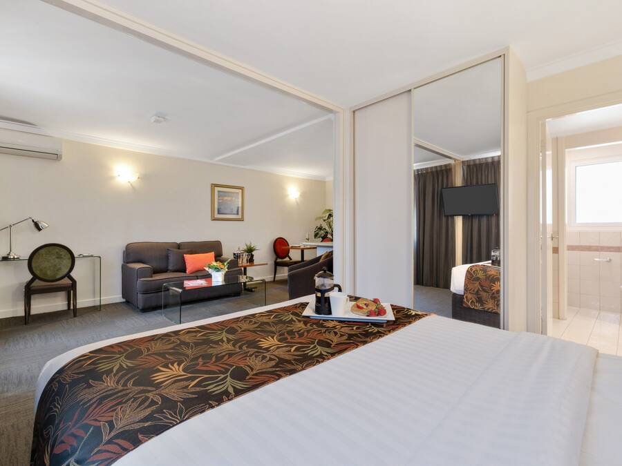 A hotel room with a large bed, a sofa, a coffee table, and a desk. There is a bathroom visible through an open door.