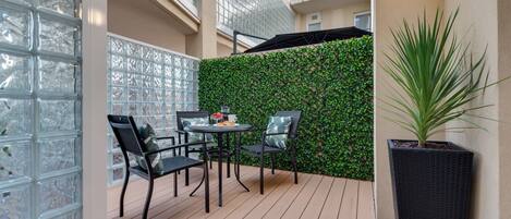 Un balcón con una barandilla de vidrio, un muro verde y una planta en maceta.