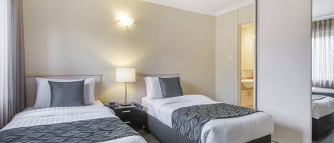 A hotel room with two beds, a nightstand, a lamp, and a mirror.