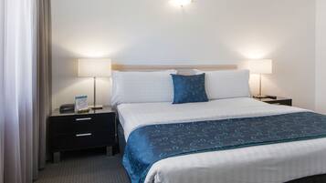 A hotel room with a neatly made bed, two bedside tables with lamps, a dark-colored dresser, and a light-colored headboard.