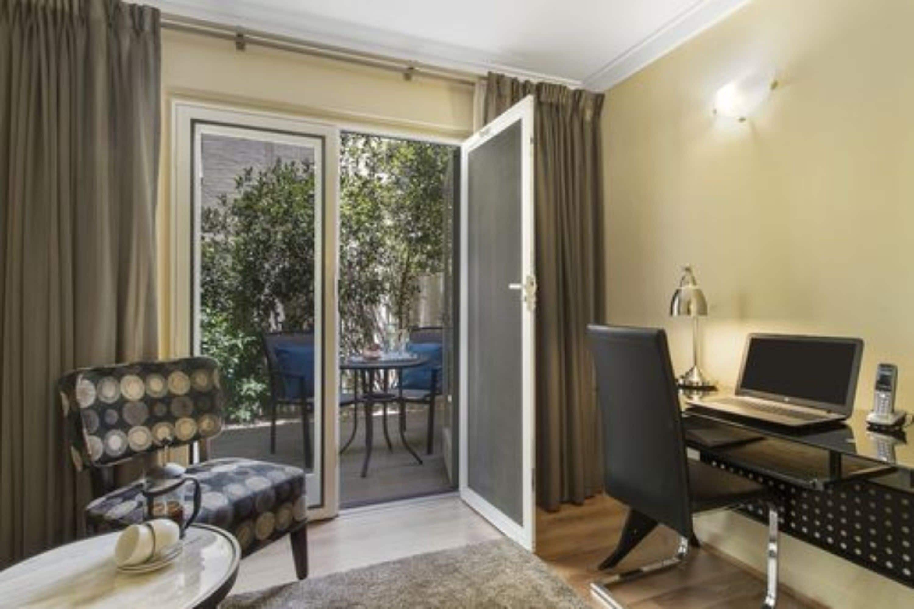 A room with a sliding glass door leading to an outdoor area, a desk with a laptop, a chair, and a small table with a vase.