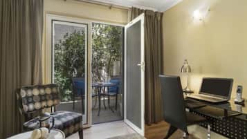 A room with a sliding glass door leading to an outdoor area, a desk with a laptop, a chair, and a small table with a vase.