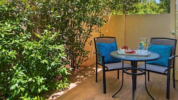 Un patio al aire libre con una mesa redonda y dos sillas, rodeado de abundante vegetación.