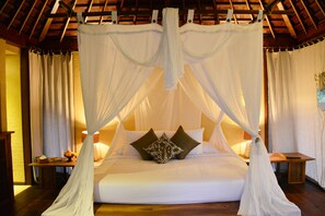 A bedroom with a canopy bed, wooden flooring, and a nightstand with a lamp. - NusaBay Menjangan by WHM (Sumberklampok)