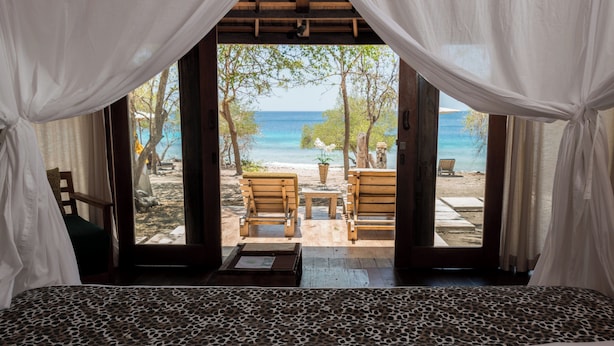 Une chambre avec vue sur la plage, comprenant un lit, une table en bois et deux chaises.