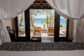 A room with a view of the beach, featuring a bed, a wooden table, and two chairs. - NusaBay Menjangan by WHM (Sumberklampok)