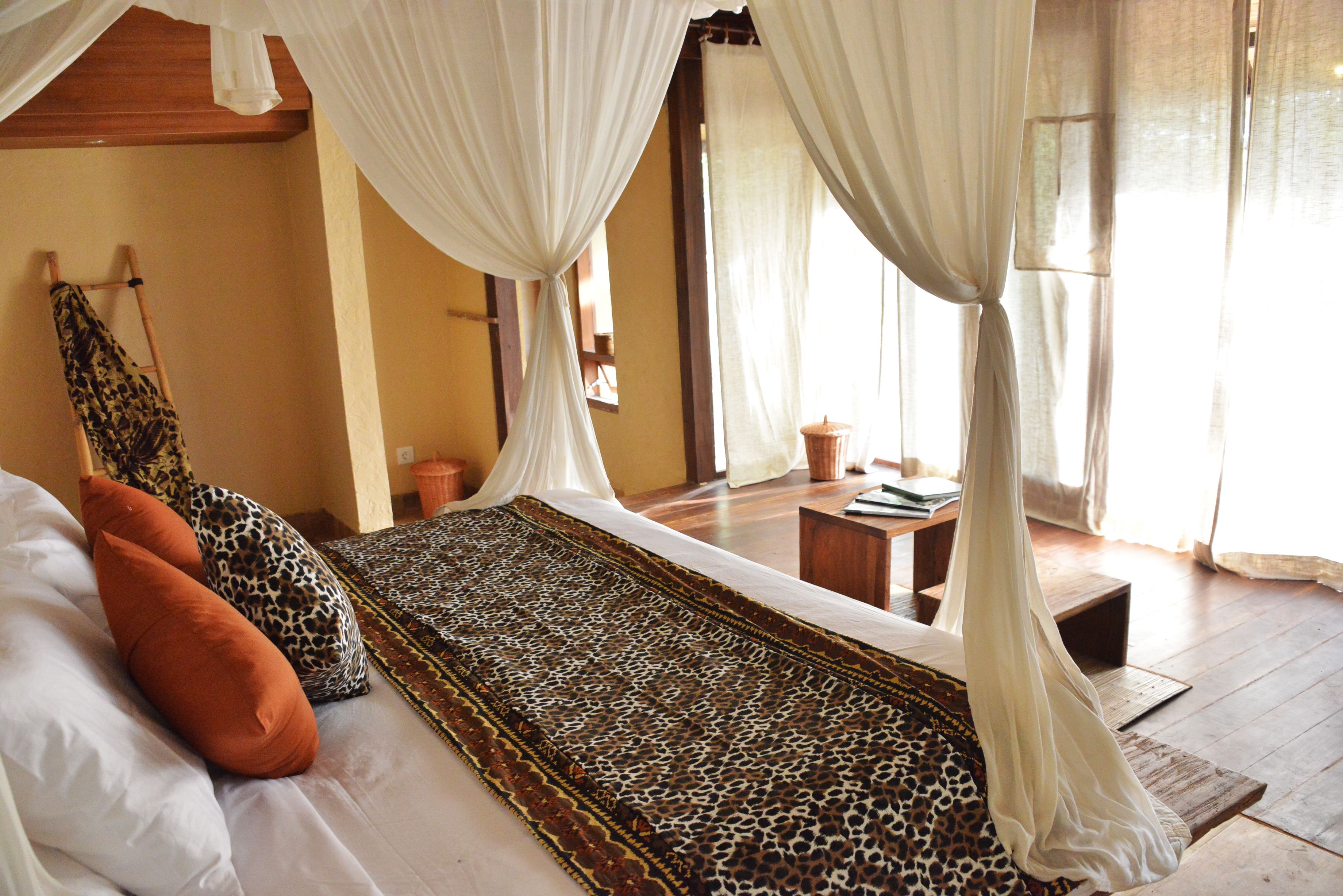 Ein Schlafzimmer mit einem Bett, einem Leopardenfell-Teppich, weißen Vorhängen und Holzboden.