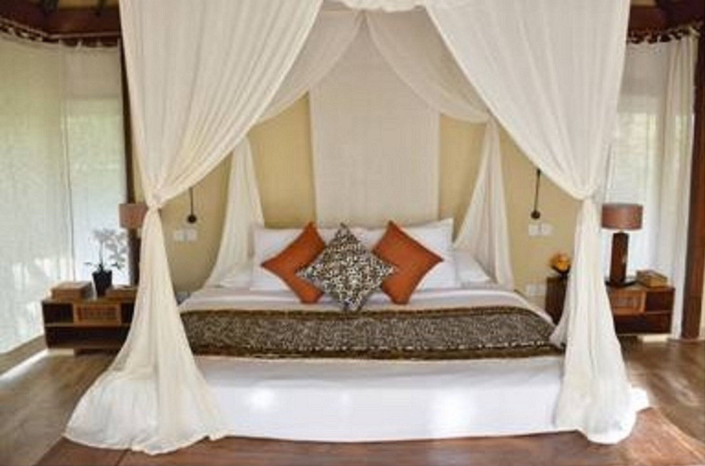 Un dormitorio con cama con dosel, cortinas blancas y suelo de madera.