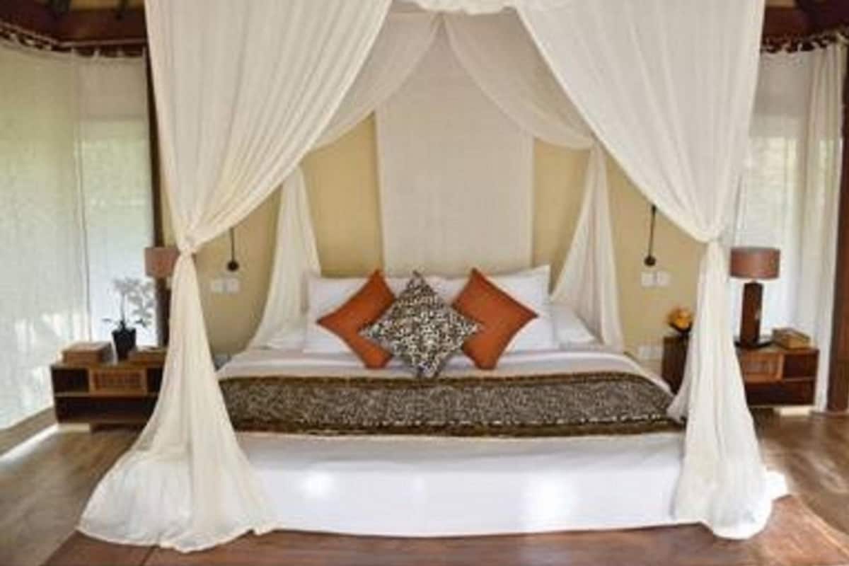Un dormitorio con cama con dosel, cortinas blancas y suelo de madera.