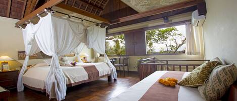 A bedroom with a canopy bed, a sofa bed, and a balcony with a view of trees.