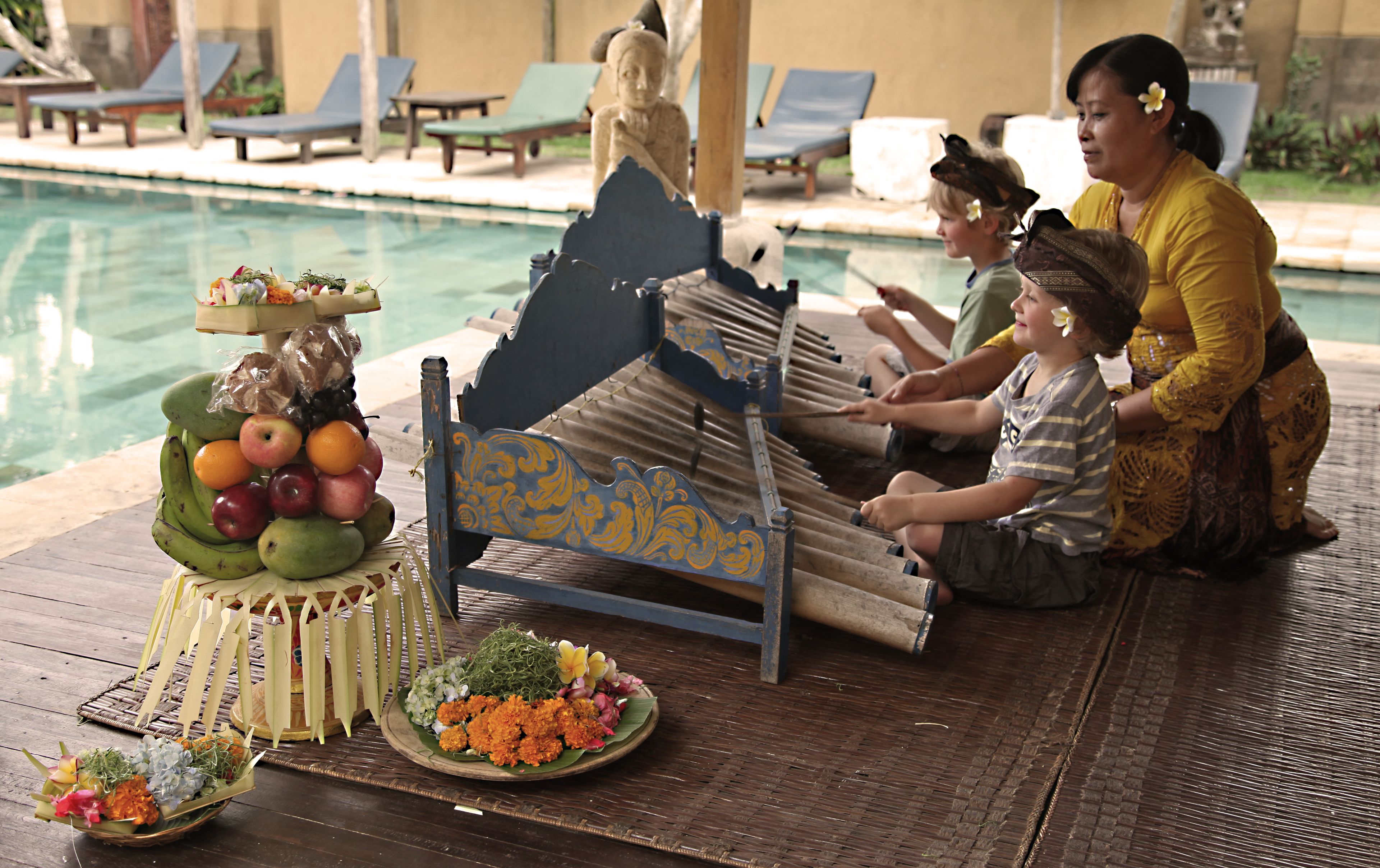 A traditional ceremony with a boat, fruit, and flowers on a wooden deck by a pool.