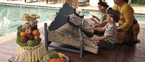 A traditional ceremony with a boat, fruit, and flowers on a wooden deck by a pool.