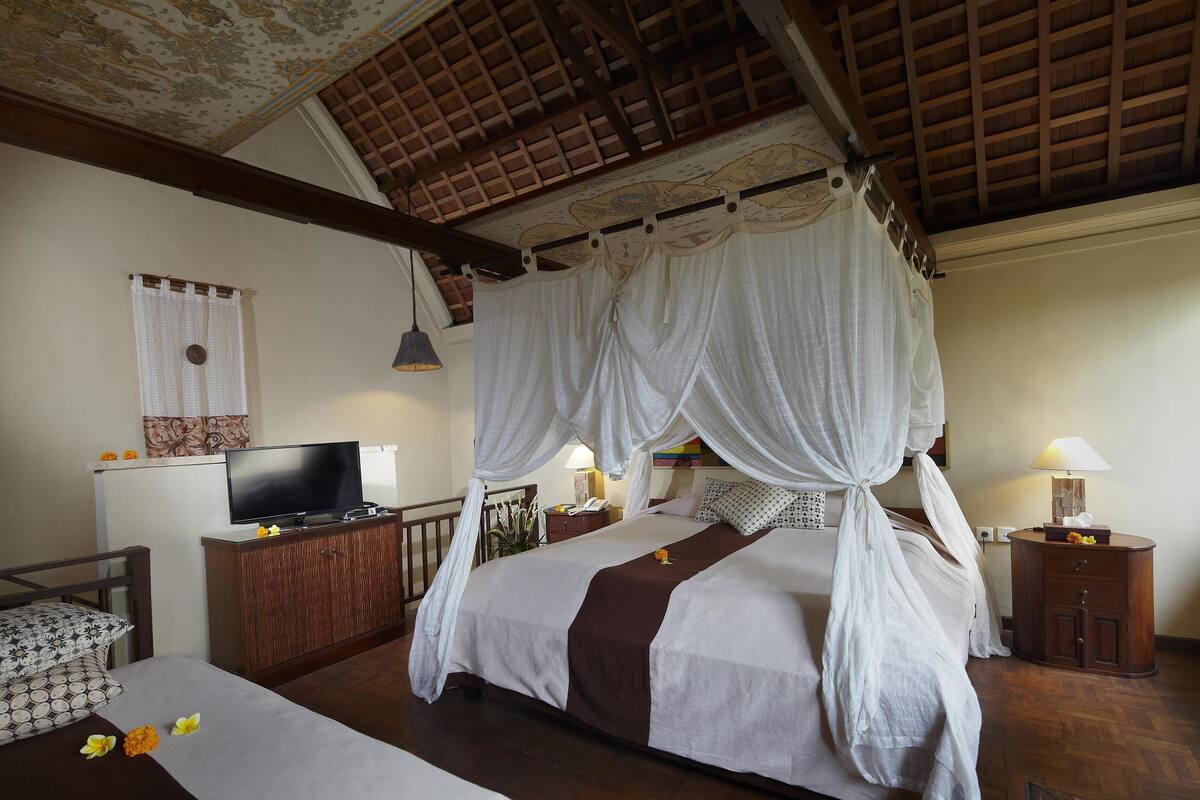 Une chambre à coucher avec un lit à baldaquin, une télévision, une table de chevet avec une lampe et une armoire en bois.