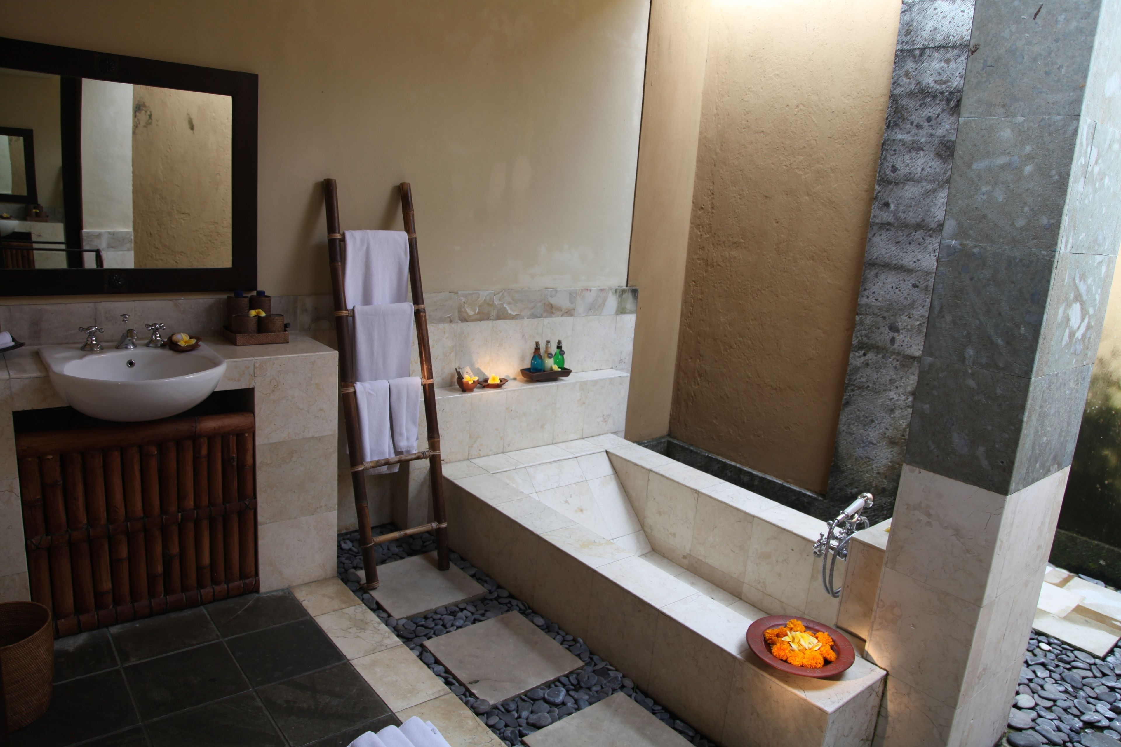 A bathroom with a large bathtub, a sink, and a mirror. There is a towel rack and a small shelf with toiletries.