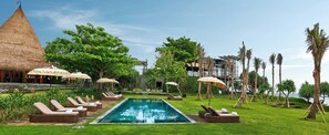 Zona junto a la piscina con sillas de descanso y sombrillas, rodeada de vegetación y vistas al mar.